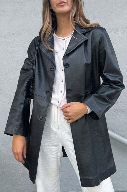 Person wearing a black leather coat over a white outfit against a gray background